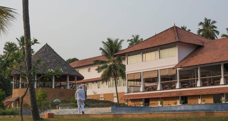 Een man in een witte outfit die loopt in de buurt van resortgebouwen en palmbomen.