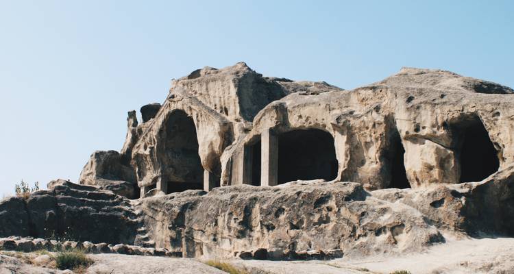 Rotsformaties en oude grotwonigen onder heldere luchten.