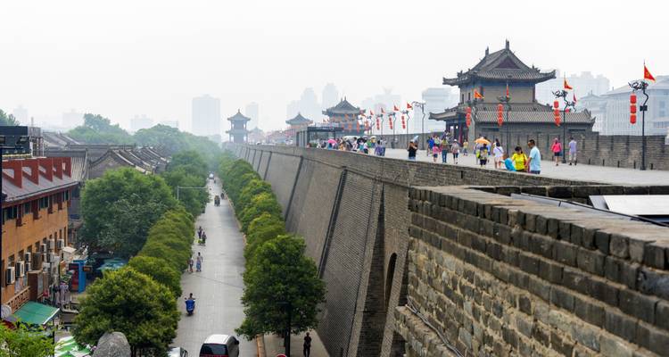 Los visitantes pasean por las antiguas murallas de piedra de la Muralla de Xi'an que dominan las calles urbanas modernas.