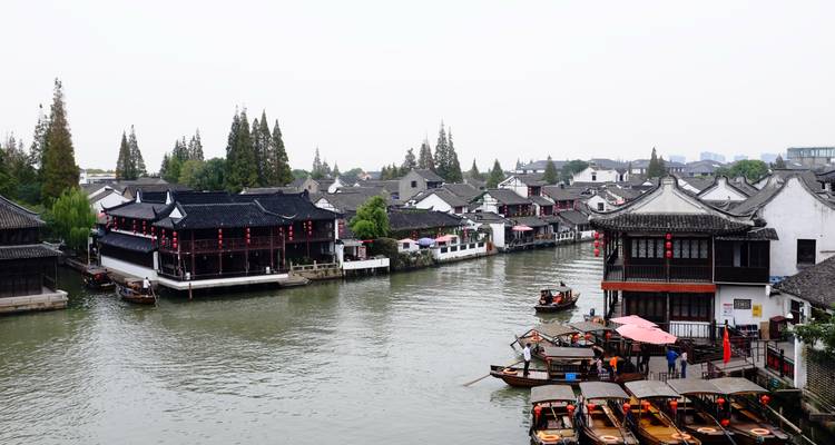 Las casas tradicionales con tejas negras bordean un canal tranquilo donde pequeñas barcas de madera transportan pasajeros en un pueblo histórico de agua.