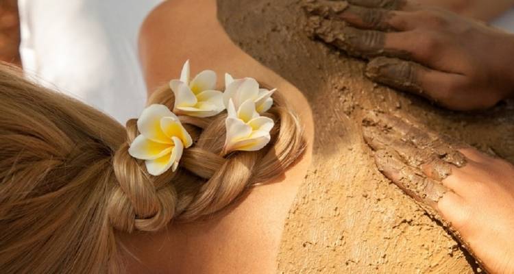 Mud therapy being applied with flowers in the hair of a person.