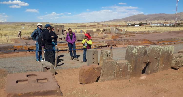 Small tour group listens to a guide among scattered carved stones at a high-altitude archaeological site.