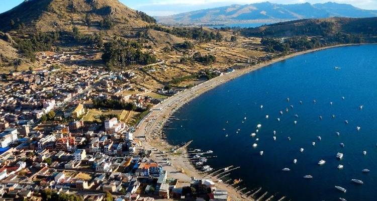 Vue aérienne de la ville de Copacabana épousant le rivage courbe du lac Titicaca parsemé de bateaux.