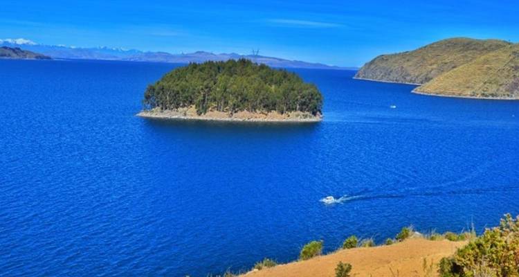 Un lac bleu éclatant entoure une minuscule île boisée avec un hors-bord qui trace un sillage.