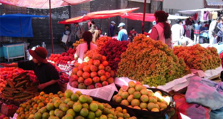 Geschäftiger Freiluftmarkt für Obst und Gemüse mit Haufen bunter Früchte unter provisorischen Zelten.