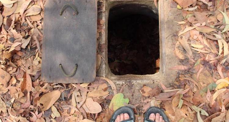 Narrow rectangular tunnel entrance set among dry leaves with traveler’s feet visible.
