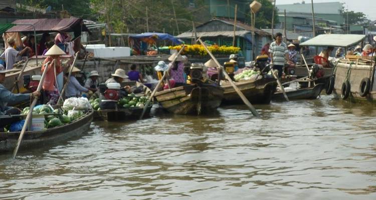Bustling floating market boats trade produce along a muddy Mekong Delta canal.