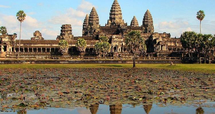 Iconic Angkor Wat towers reflect in a lily-covered pool under bright blue skies.