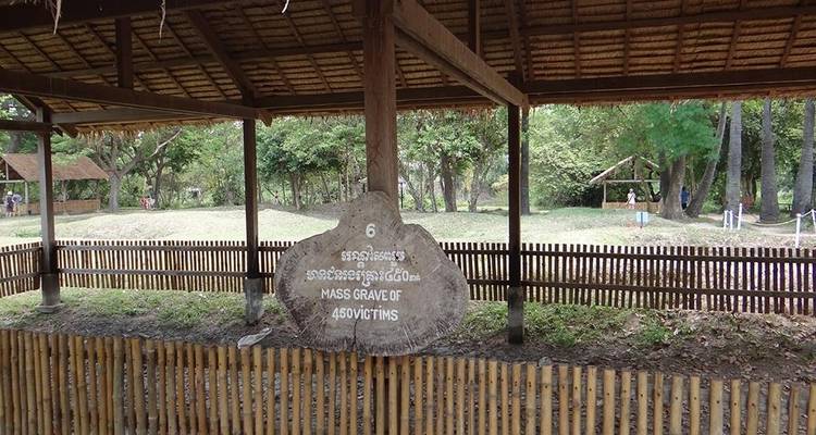 Wooden sign marks a mass grave site within the Killing Fields memorial, surrounded by fencing.