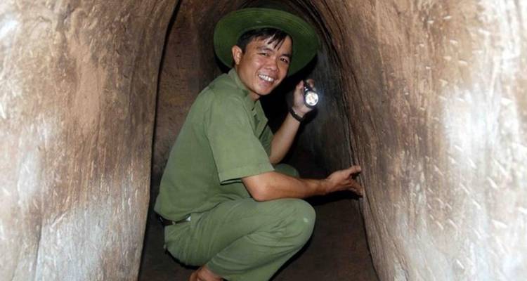 Guide smiles while crouched inside the narrow Cu Chi tunnel holding a flashlight.