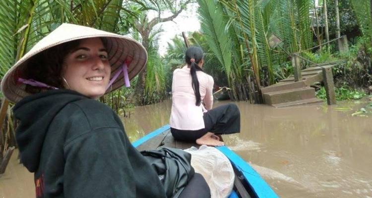 Deux personnes sont assises dans un étroit canoë en bois qui glisse dans les canaux boueux bordés de palmiers d'un delta tropical.