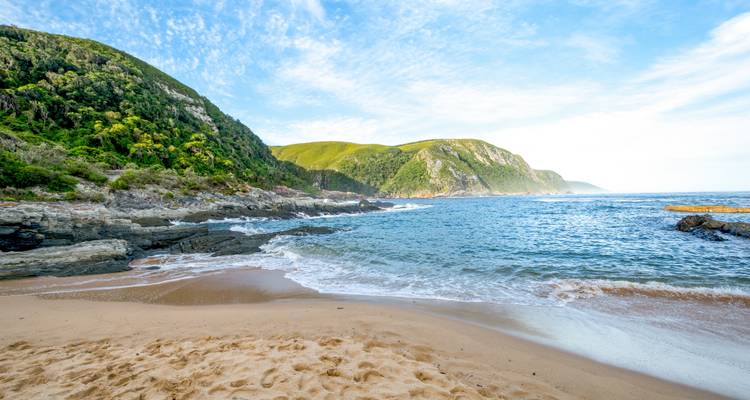 Beach with waves crashing on the shore and green hills in the background.