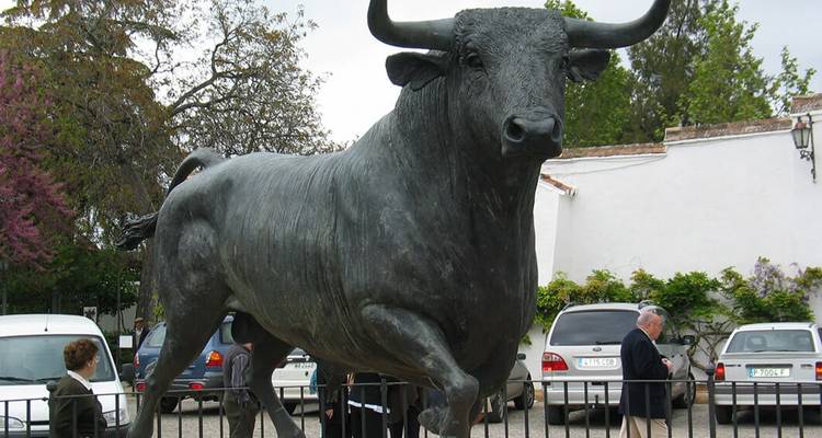 Une grande statue de taureau avec des touristes à proximité.