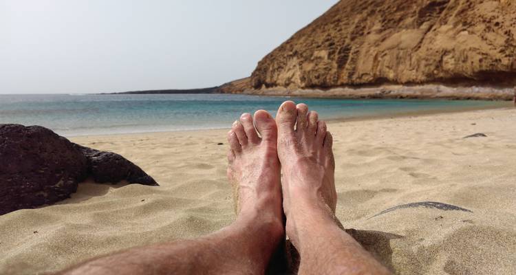 Vista de pies descalzos en una playa con un acantilado rocoso al fondo.