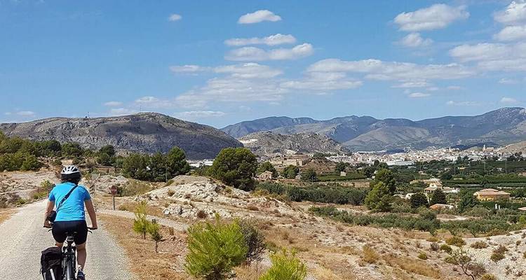 Ein Radfahrer auf einem Weg mit Blick auf eine hügelige Landschaft mit einer Stadt.