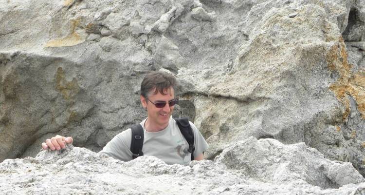 Homme posant avec des rochers dans une région montagneuse.