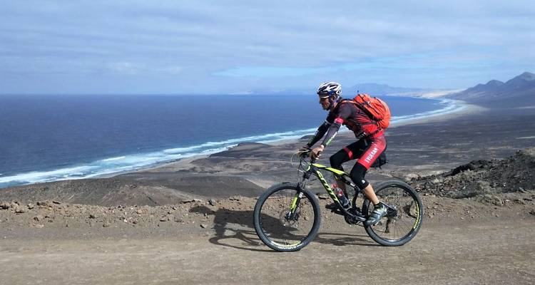 Mountain biker pedals along a dusty ridge with sweeping views over the Atlantic shoreline.