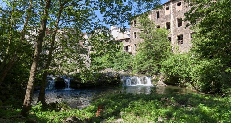 Kleiner Wasserfall mit einem alten Gebäude, umgeben von Grün.