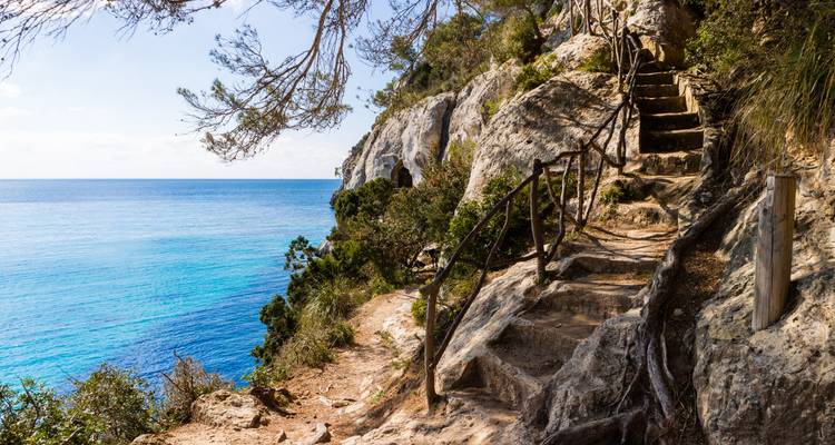 Sentier côtier avec marches rocheuses et mer bleue claire.