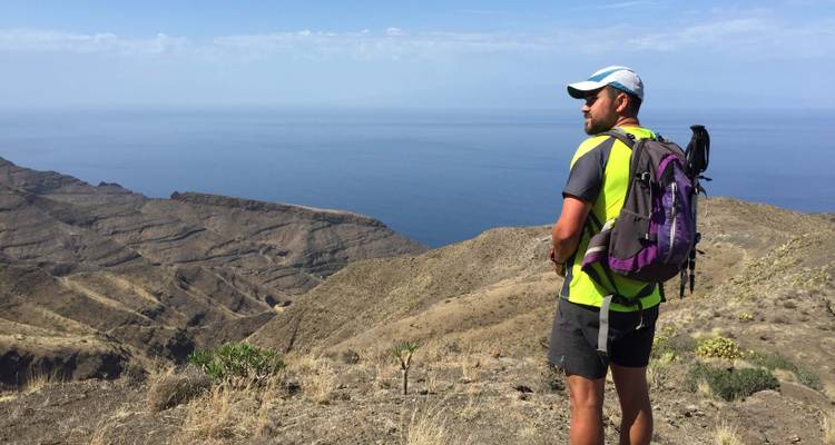 Randonneur debout sur une montagne surplombant un vaste paysage océanique.