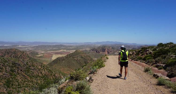 Randonneur marchant sur un sentier avec une vue panoramique sur les montagnes en arrière-plan.