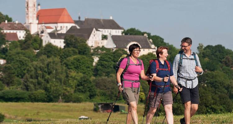 Trois randonneurs marchant vers un monastère pittoresque.