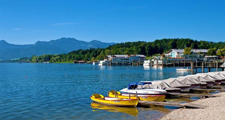 Un lac avec un ponton et des bateaux, entouré de montagnes et de forêts.