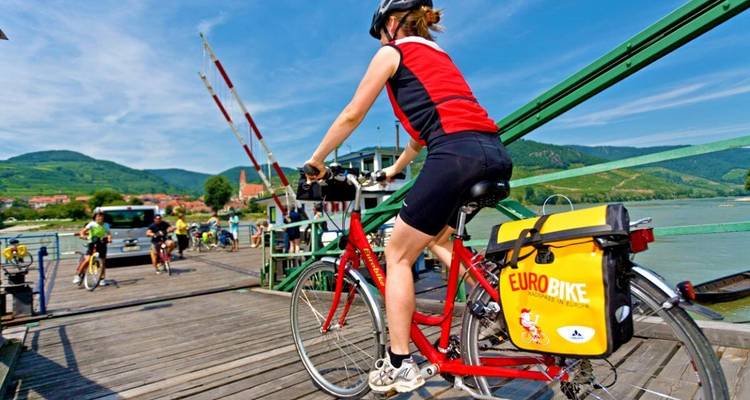 Radfahrer, die eine Fähre besteigen, mit malerischen Ausblicken im Hintergrund.