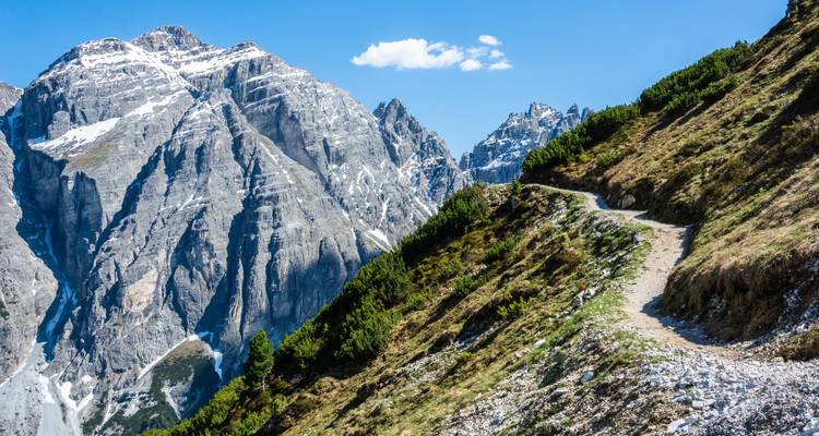 Bergpfad mit schroffen Gipfeln und blauem Himmel.