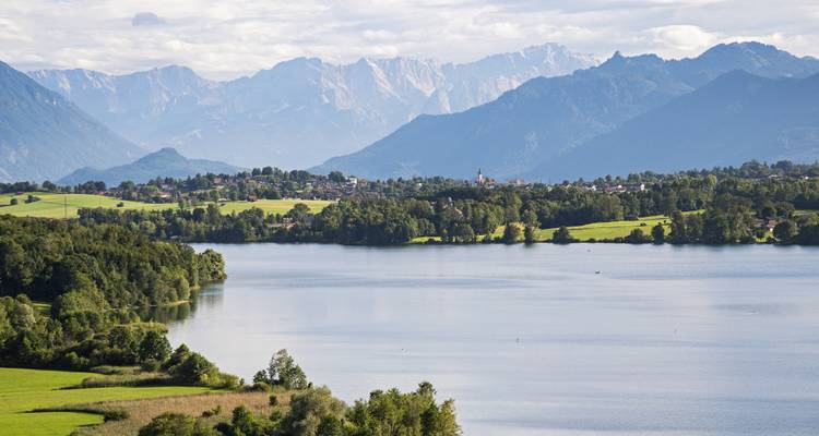 Lago amplio con campiña ondulada y cordillera alpina distante