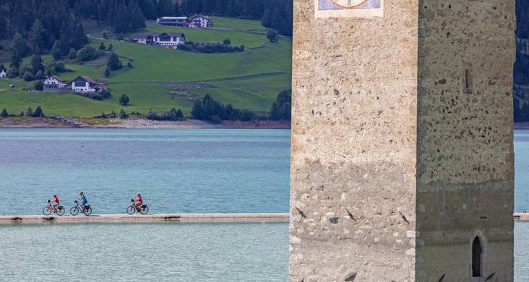 Radfahrer, die an einem versunkenen Kirchturm in einem See vorbeifahren.