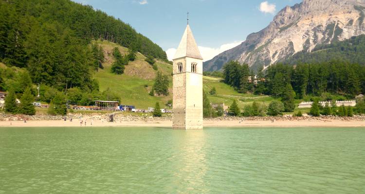 Een ondergedompelde kerktoren in een meer met bergen op de achtergrond.