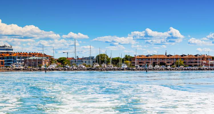 Blick vom Wasser auf eine Küstenstadt mit niedrigen Gebäuden und einem strahlend blauen Himmel über sanften Wellen.