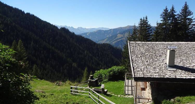 Cabane rustique entourée de collines boisées avec des montagnes au loin.