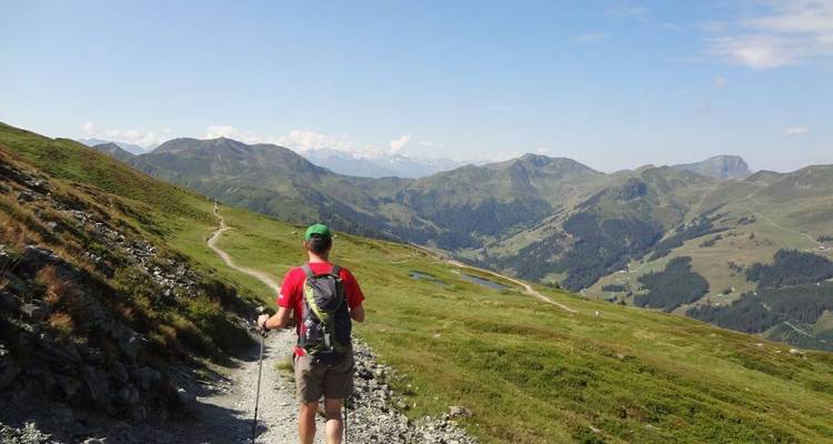 Randonneur marchant le long d'un sentier de montagne sous un ciel dégagé.