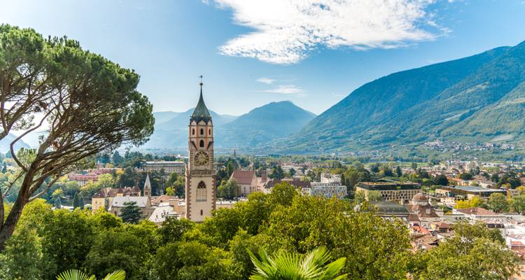 Paysage urbain de Merano avec une tour d'horloge et des montagnes.