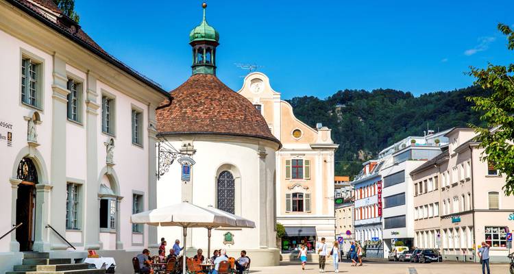 Gente sentada fuera de un edificio histórico en una plaza del pueblo.