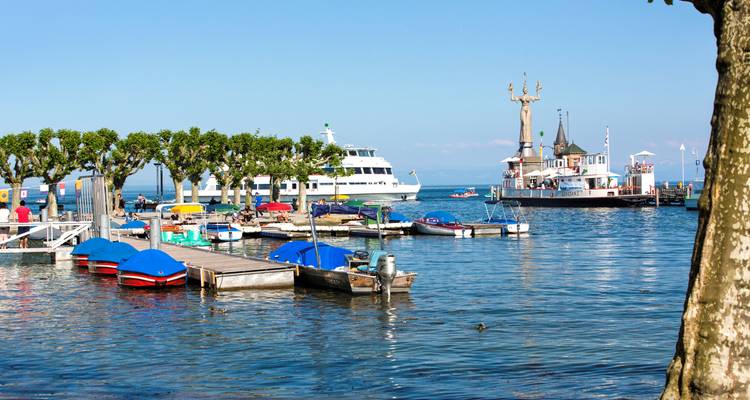 Vista del puerto con barcos y un ferry cerca de una estatua en el lago.