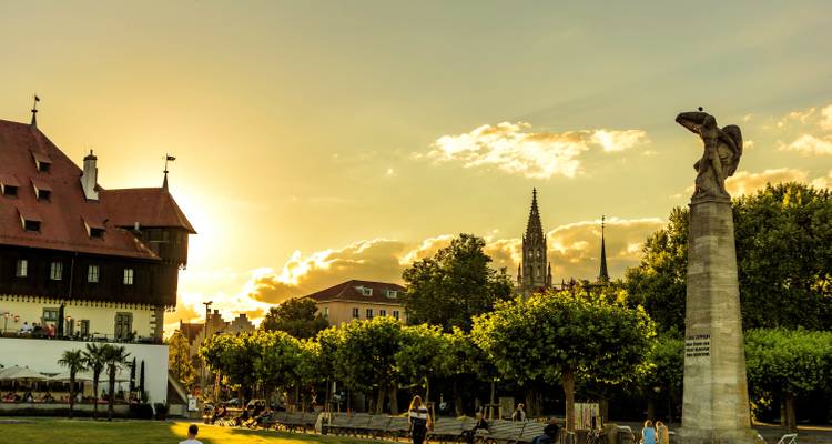Vista del atardecer de una estatua en un parque con un paisaje urbano de fondo.