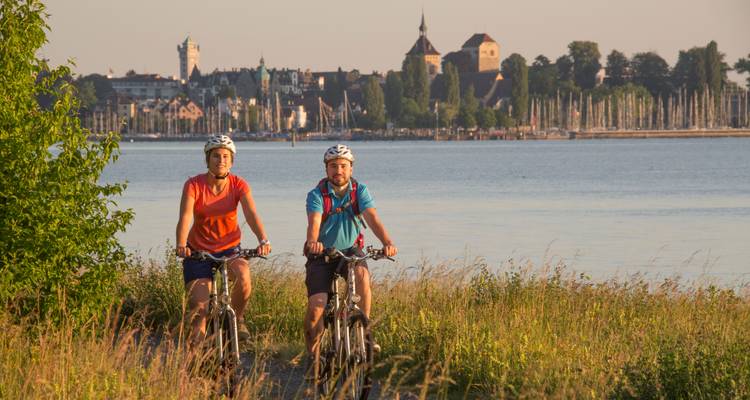 Stel dat fietst op een groen pad langs het meer met een historisch stadje en jachthaven aan de overkant in het gouden licht.
