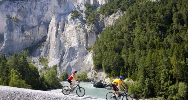 Ciclistas montando a lo largo de un río a través de un paisaje montañoso.
