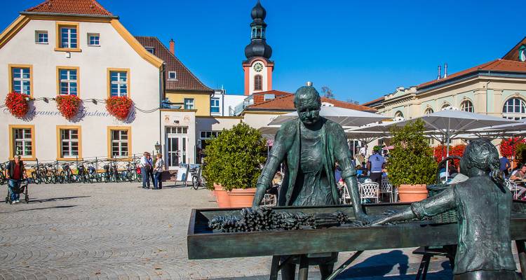 Place de marché en plein air avec une statue, des fleurs et des bâtiments historiques.