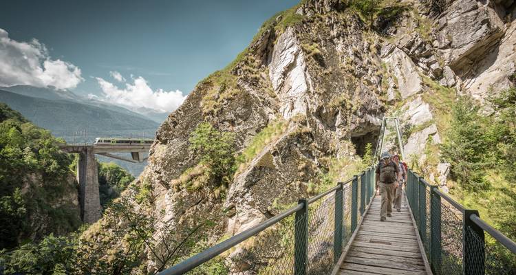 Des gens traversent un pont dans un paysage montagneux rocheux.