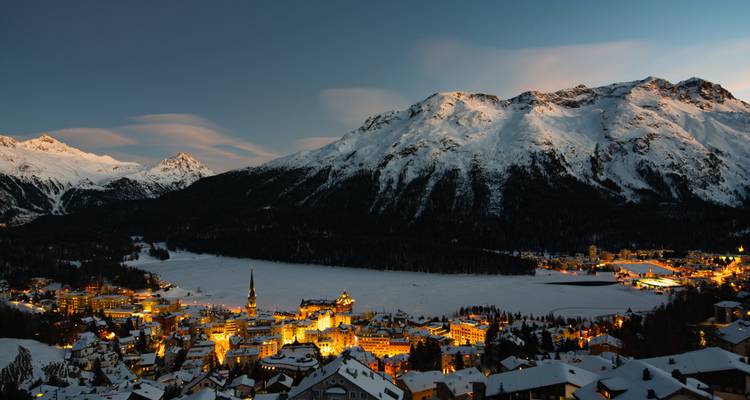 Scène nocturne de montagne enneigée avec village illuminé.