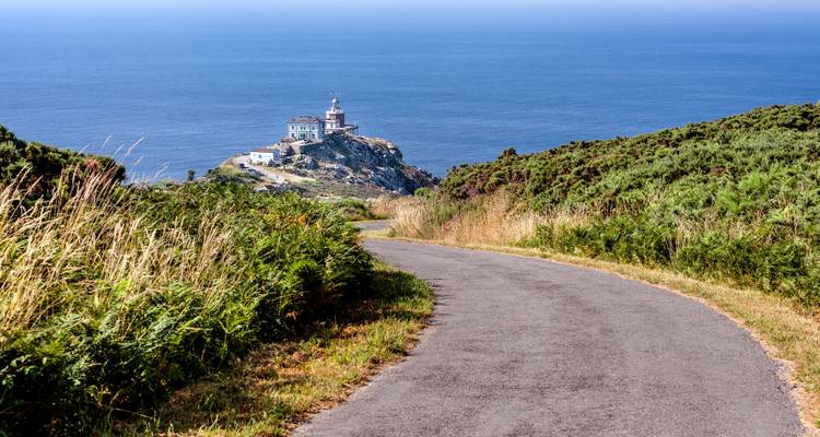 Eine gewundene Straße, die zu einem Leuchtturm auf einem Küstenhügel führt.