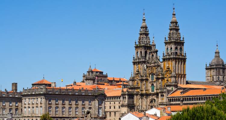 Ein Blick auf die Kathedrale von Santiago de Compostela mit ihren verzierten Türmen und roten Dächern vor einem klaren blauen Himmel.