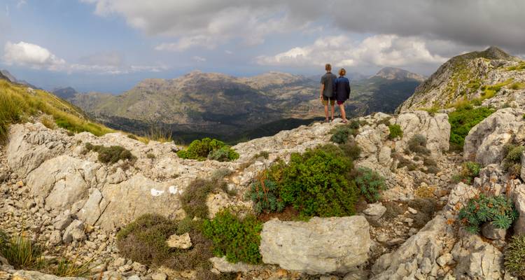 Deux personnes debout au sommet d'une montagne rocheuse avec vue sur les vallées et les montagnes.