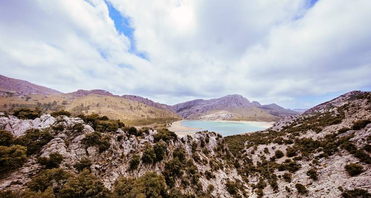 Un paysage rocheux menant à une étendue d'eau sereine sous un ciel nuageux.