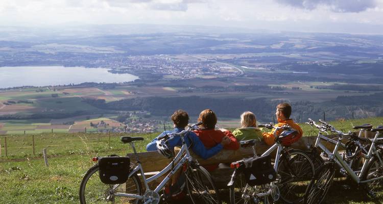 Gruppe von Radfahrern, die auf einer Bank mit Panoramablick auf Felder und einen See ruhen.