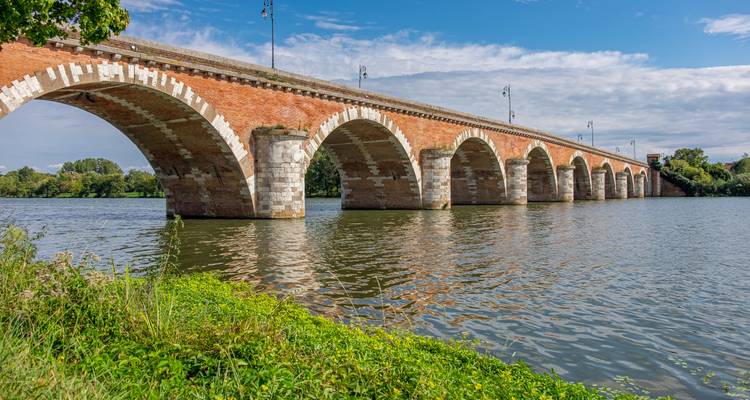 Pont en briques enjambant une rivière, entouré de verdure.